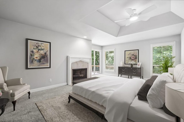 bedroom featuring baseboards, a high end fireplace, a raised ceiling, carpet flooring, and ceiling fan