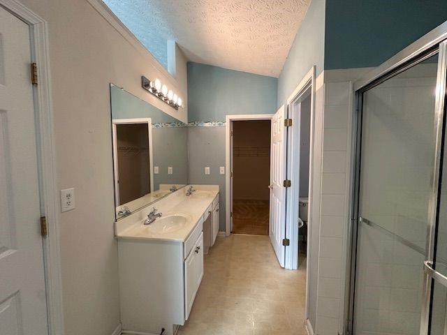 bathroom with lofted ceiling, a spacious closet, double vanity, and a textured ceiling