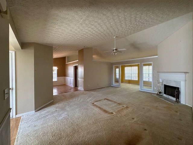 unfurnished living room with light carpet, a ceiling fan, a textured ceiling, a high end fireplace, and lofted ceiling