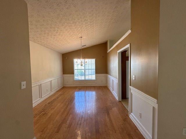 unfurnished dining area featuring a wainscoted wall, lofted ceiling, wood finished floors, a decorative wall, and a textured ceiling