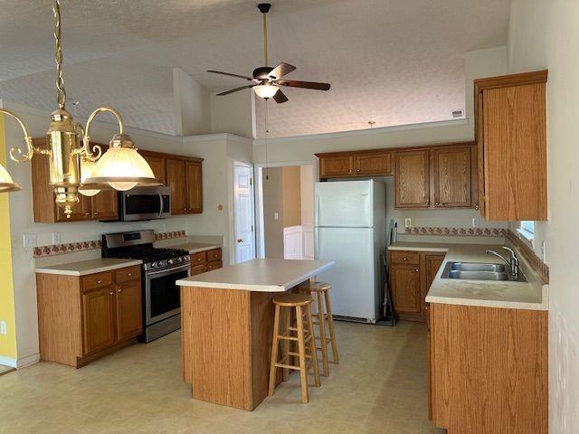 kitchen featuring light floors, a sink, stainless steel appliances, brown cabinets, and a center island