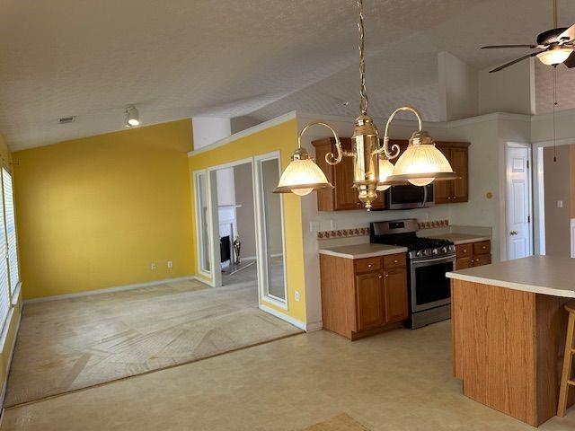 kitchen with brown cabinets, stainless steel appliances, light countertops, ceiling fan, and vaulted ceiling