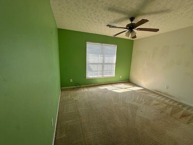 carpeted empty room with visible vents, a textured ceiling, baseboards, and a ceiling fan