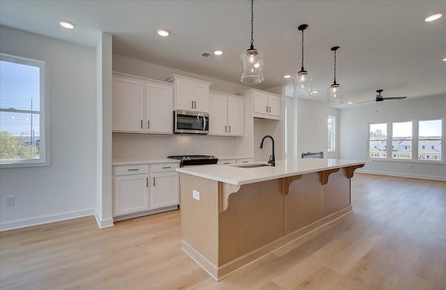 1919 Deco Dr, Kennesaw, GA 30144 - kitchen featuring stainless steel microwave, ceiling fan, light wood-style floors, a kitchen breakfast bar, and an island with sink