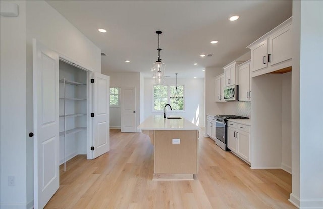 1919 Deco Dr, Kennesaw, GA 30144 - kitchen featuring stainless steel appliances, a center island with sink, white cabinetry, light countertops, and light wood finished floors