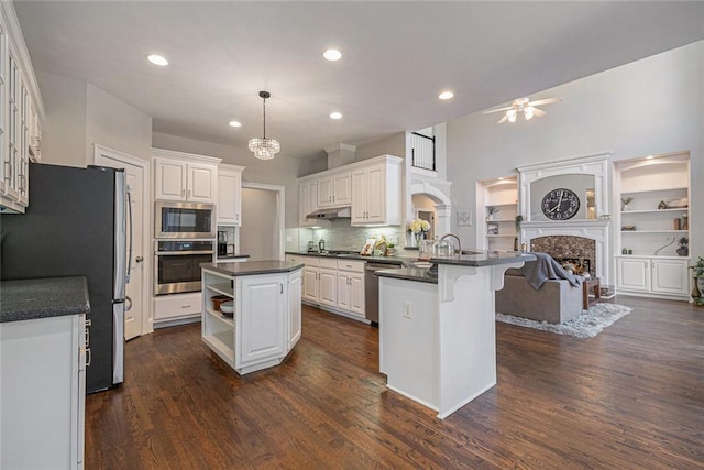 kitchen with dark countertops, a kitchen island with sink, stainless steel appliances, white cabinetry, and pendant lighting