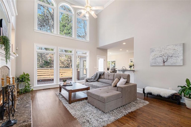 living room with dark wood-style floors, a lit fireplace, baseboards, and a ceiling fan