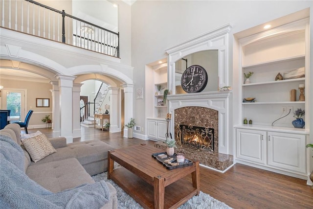 living room featuring built in shelves, arched walkways, dark wood-style floors, a fireplace, and ornate columns