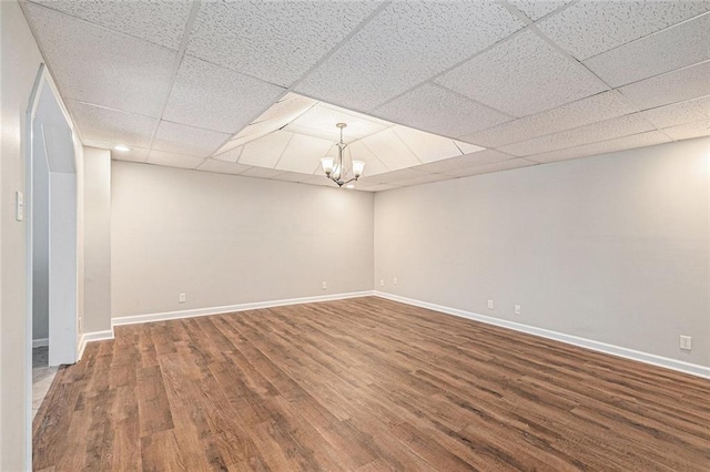 empty room with a chandelier, a paneled ceiling, baseboards, and wood finished floors