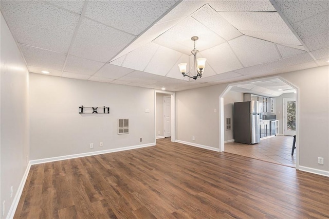 below grade area with baseboards, wood finished floors, freestanding refrigerator, a paneled ceiling, and a chandelier