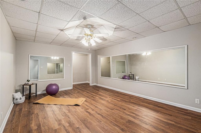 workout area featuring a ceiling fan, baseboards, a drop ceiling, and wood finished floors