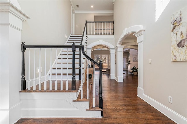 interior space with arched walkways, decorative columns, a towering ceiling, wood finished floors, and baseboards