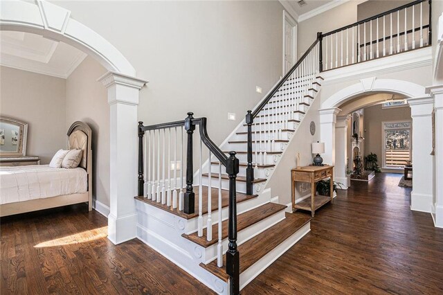 foyer with ornamental molding, arched walkways, dark wood-style flooring, and decorative columns