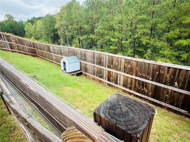 view of yard featuring an outdoor structure, a fenced backyard, and a wooded view