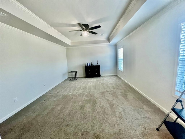 unfurnished living room featuring a raised ceiling, ornamental molding, carpet floors, baseboards, and ceiling fan