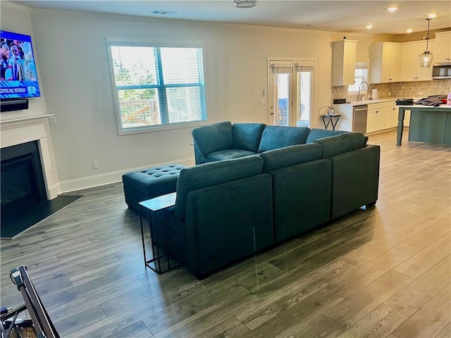 living area with wood finished floors, visible vents, baseboards, a fireplace with flush hearth, and crown molding