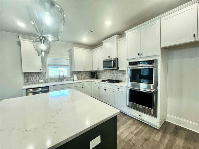 kitchen featuring a sink, backsplash, wood finished floors, white cabinetry, and appliances with stainless steel finishes