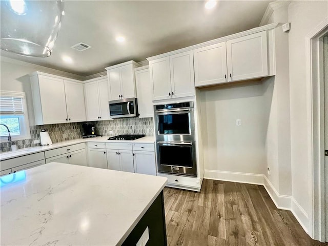 kitchen featuring visible vents, a sink, stainless steel appliances, white cabinets, and backsplash