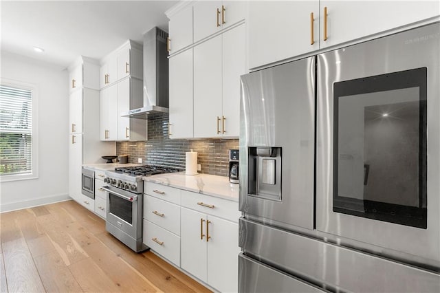 343 Concord St, Alpharetta, GA 30009 - kitchen featuring wall chimney range hood, appliances with stainless steel finishes, light wood finished floors, decorative backsplash, and white cabinets