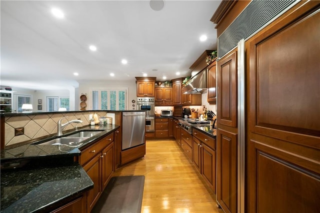 kitchen featuring sink, dark stone counters, stainless steel appliances, a healthy amount of sunlight, and light wood-type flooring