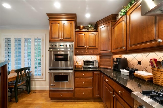 kitchen featuring crown molding, light hardwood / wood-style flooring, dark stone countertops, double oven, and decorative backsplash