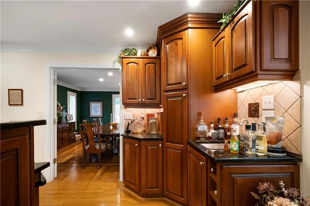 kitchen featuring ornamental molding, dark stone countertops, backsplash, and light wood-type flooring