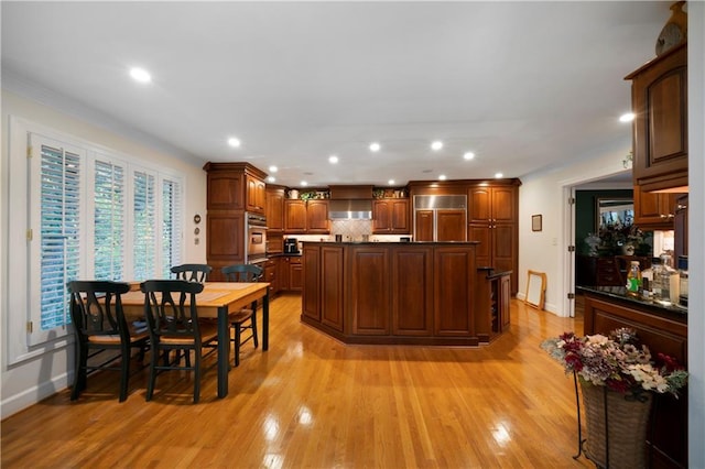 kitchen featuring stainless steel oven, a center island, paneled fridge, light hardwood / wood-style floors, and decorative backsplash