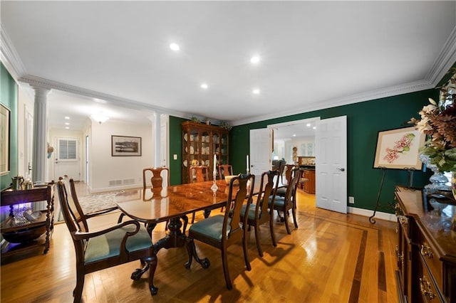 dining area featuring light wood-type flooring, ornamental molding, and ornate columns