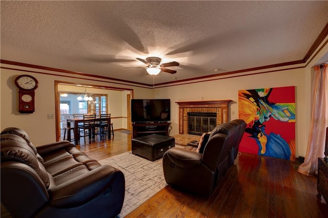 living room with ceiling fan with notable chandelier, hardwood / wood-style flooring, a textured ceiling, and a brick fireplace