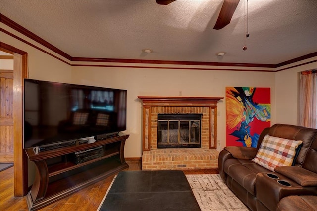 living room with hardwood / wood-style floors, ceiling fan, ornamental molding, a fireplace, and a textured ceiling