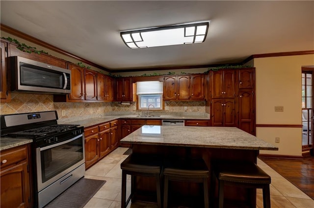 kitchen featuring stainless steel appliances, light tile patterned floors, a kitchen island, a breakfast bar area, and ornamental molding