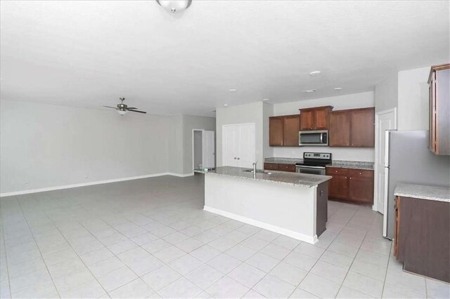 kitchen featuring ceiling fan, light stone counters, an island with sink, sink, and appliances with stainless steel finishes