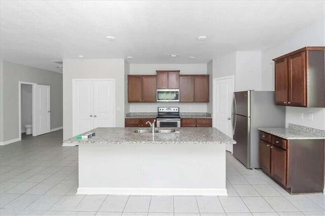 kitchen featuring appliances with stainless steel finishes, light tile patterned flooring, an island with sink, and light stone counters