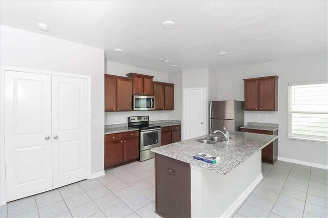 kitchen featuring an island with sink, sink, light tile patterned floors, and stainless steel appliances