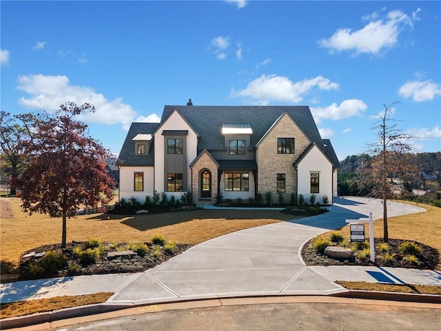 view of front of house with driveway, stone siding, and a front lawn