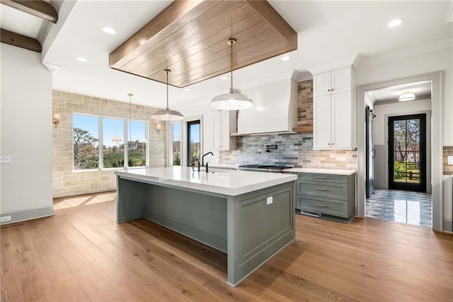 kitchen featuring light countertops, light wood finished floors, tasteful backsplash, white cabinetry, and wall chimney range hood