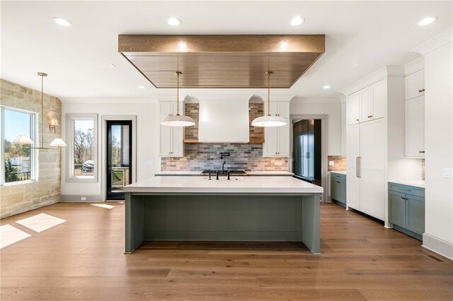 kitchen featuring light countertops, white cabinets, light wood finished floors, wall chimney exhaust hood, and backsplash