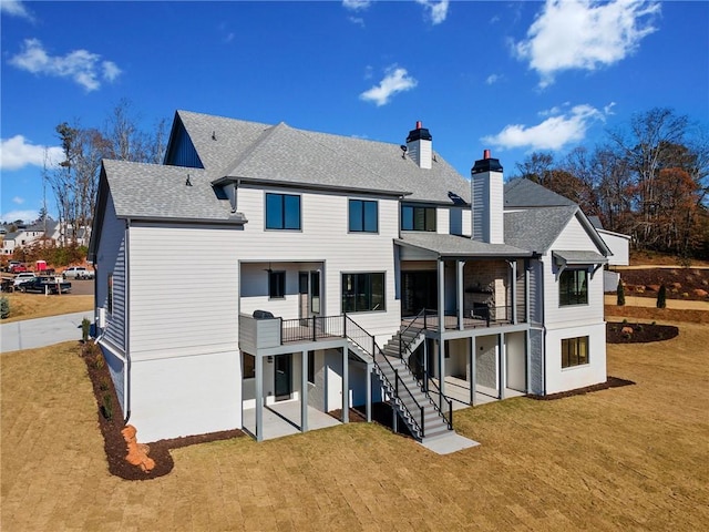 back of house featuring a chimney, stairway, roof with shingles, a yard, and a patio area