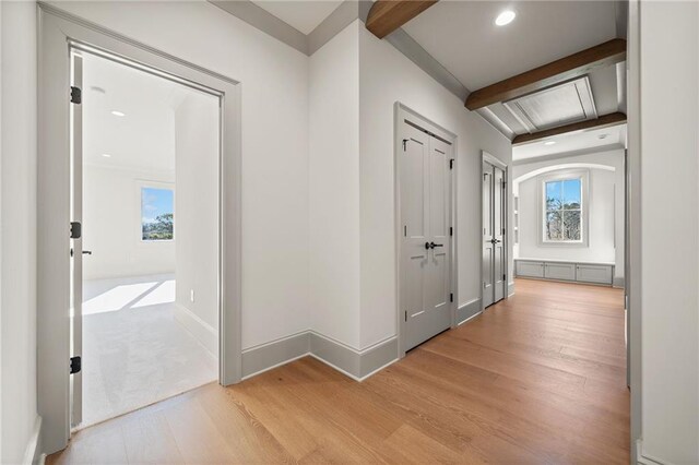 hallway featuring baseboards, beamed ceiling, light wood-style floors, and a healthy amount of sunlight