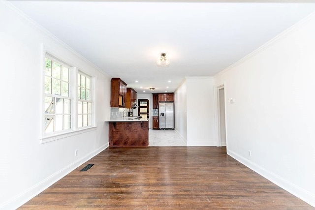 unfurnished living room featuring visible vents, ornamental molding, baseboards, and wood finished floors