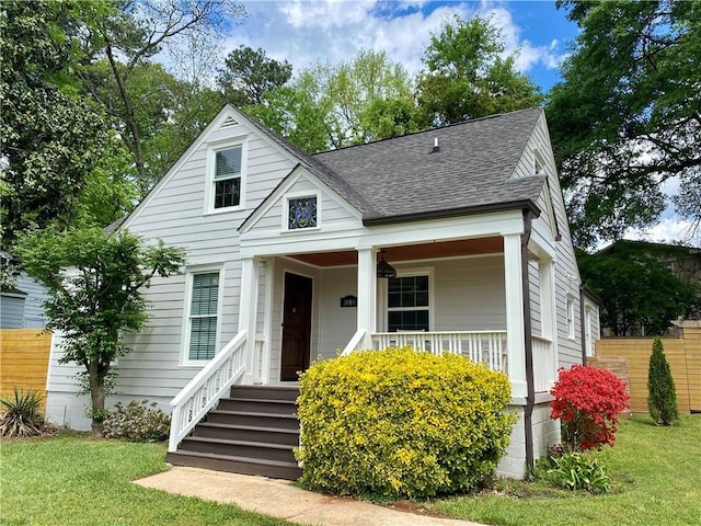 bungalow-style home with a porch, fence, a shingled roof, and a front yard