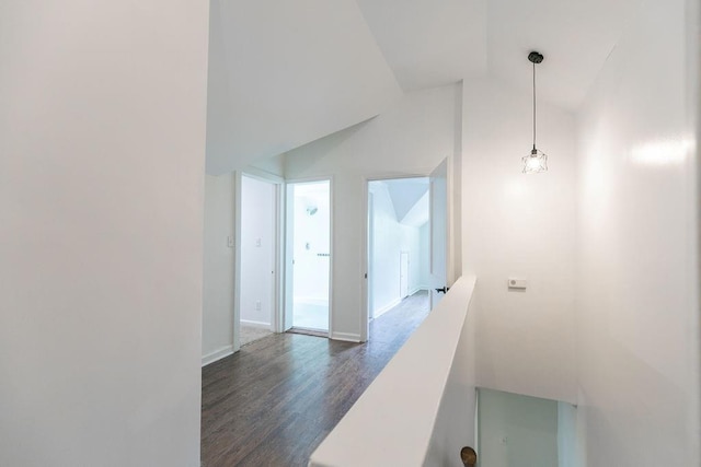 hallway featuring dark wood-type flooring, baseboards, vaulted ceiling, and an upstairs landing