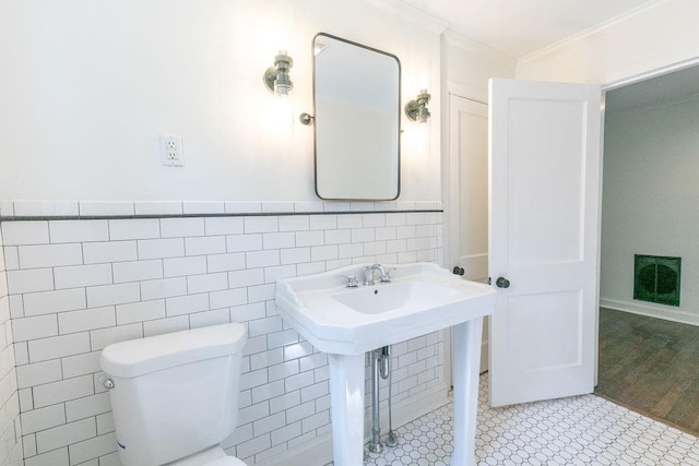 half bathroom with crown molding, tile walls, wainscoting, a sink, and toilet