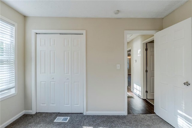unfurnished bedroom with baseboards, visible vents, dark carpet, and a closet