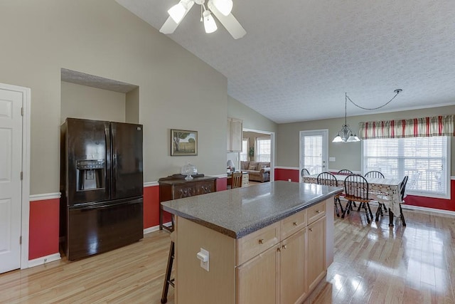 kitchen featuring hanging light fixtures, black fridge, a center island, light brown cabinetry, and dark countertops