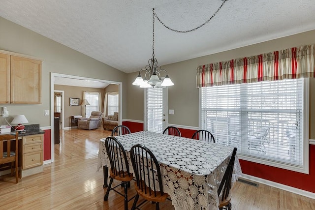 dining area with lofted ceiling, an inviting chandelier, light wood-style flooring, and a textured ceiling