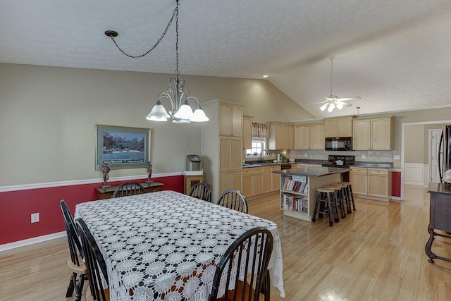 dining area featuring light wood finished floors, baseboards, vaulted ceiling, a textured ceiling, and ceiling fan with notable chandelier