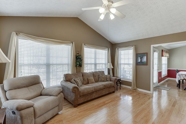 living area with baseboards, a ceiling fan, vaulted ceiling, a textured ceiling, and light wood-type flooring