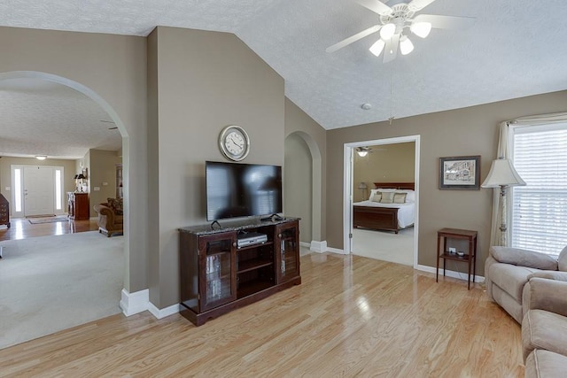 living area with arched walkways, ceiling fan, a textured ceiling, baseboards, and light wood-type flooring