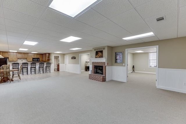 unfurnished living room featuring a wainscoted wall, a fireplace, a paneled ceiling, visible vents, and light carpet